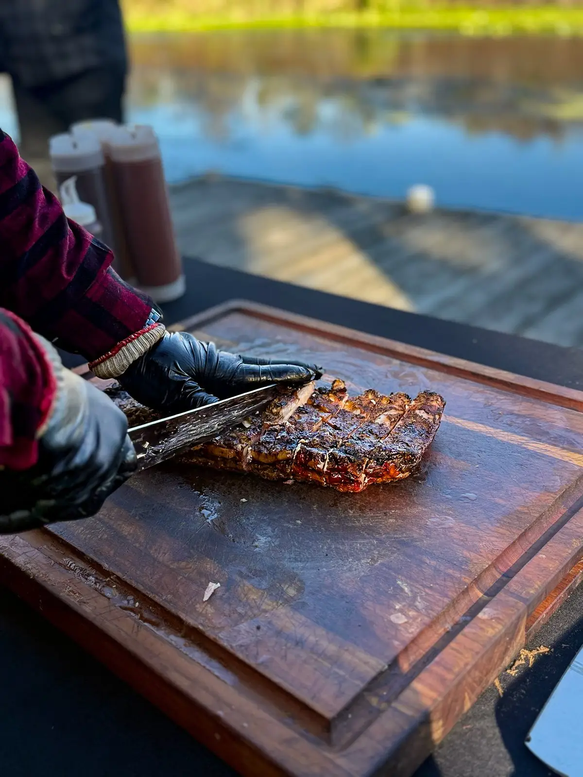 Willieboy's pitmaster slicing smoked ribs on a cutting board at a lakeside event
